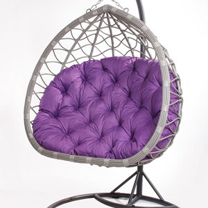 May include: A gray wicker egg chair with a tufted purple cushion. The chair hangs from a black metal frame with a circular base. The chair is designed for outdoor or indoor use.