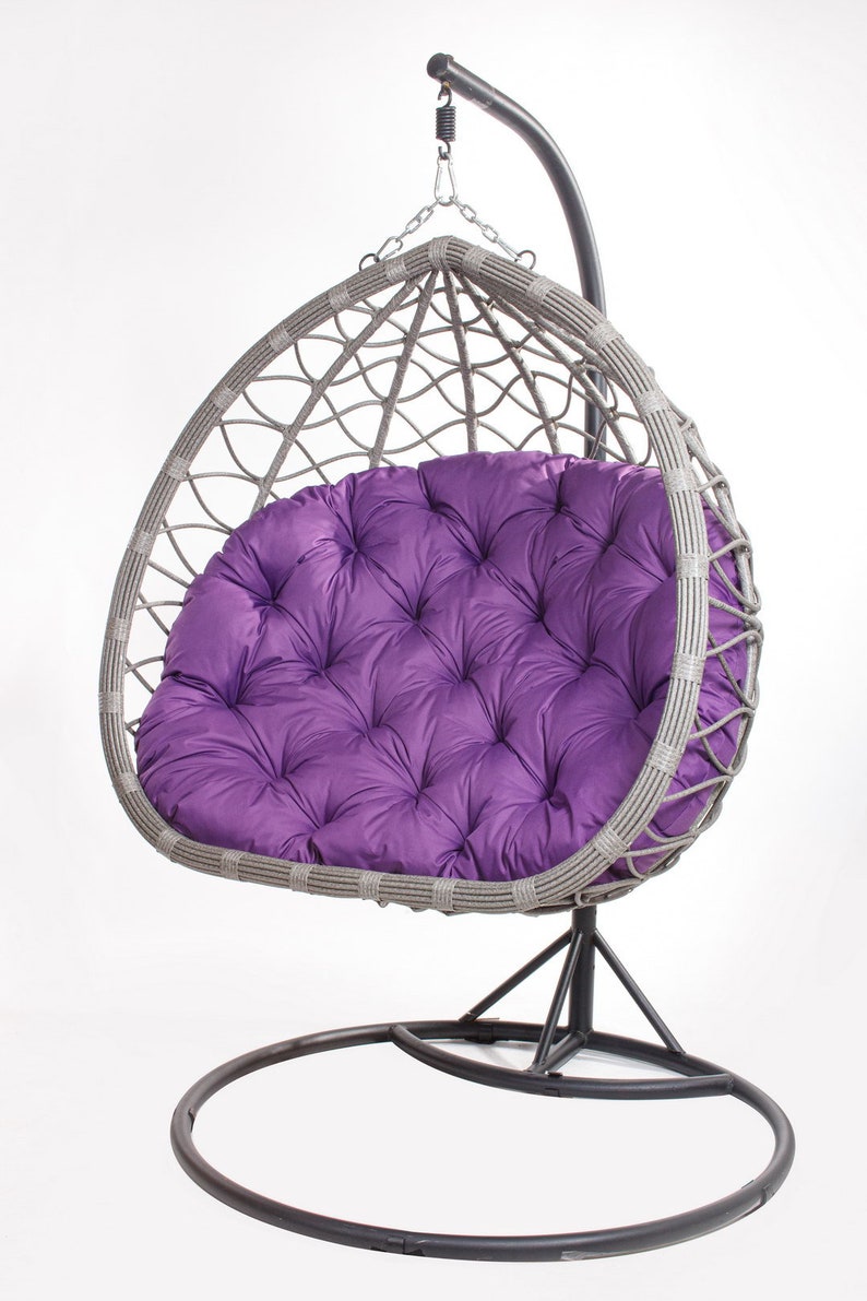 May include: A gray wicker egg chair with a tufted purple cushion. The chair hangs from a black metal frame with a circular base. The chair is designed for outdoor or indoor use.