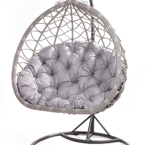 May include: A gray wicker egg-shaped hanging chair with a plush, tufted gray cushion. The chair hangs from a curved metal stand with a circular base. The design is suitable for indoor or outdoor use.