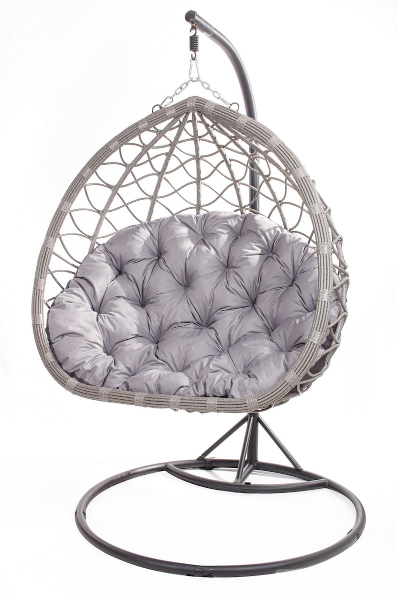 May include: A gray wicker egg-shaped hanging chair with a plush, tufted gray cushion. The chair hangs from a curved metal stand with a circular base. The design is suitable for indoor or outdoor use.