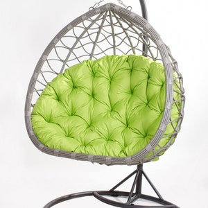 May include: A gray wicker egg chair with a bright green tufted cushion. The chair hangs from a metal frame with a circular base. The chair is designed for outdoor or indoor use.