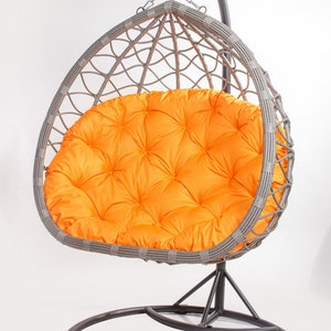 May include: A gray wicker egg chair with a bright orange cushion. The chair hangs from a curved metal stand with a circular base. The cushion has a tufted design.