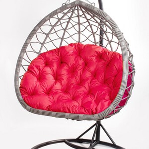 May include: A gray wicker egg chair with a vibrant red cushion. The chair hangs from a black metal frame with a circular base. The cushion is tufted and adds a pop of color to the neutral tones of the chair.