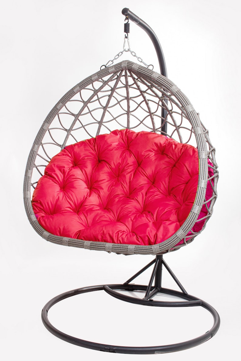 May include: A gray wicker egg chair with a vibrant red cushion. The chair hangs from a black metal frame with a circular base. The cushion is tufted and adds a pop of color to the neutral tones of the chair.