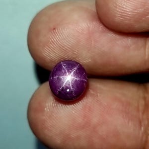 Può includere: Una pietra preziosa di rubino stella rotonda, di colore viola, con una stella a sei punte al centro.