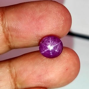 以下が含まれることがあります： 中心に6つのポイントを持つ星が描かれた、丸い紫色のスターサファイアの宝石です。