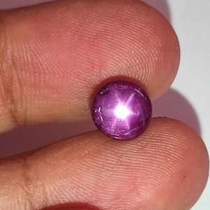 Puede incluir: Una piedra preciosa de rubí estrella redonda, en cabujón, de color púrpura con una estrella de seis puntas.