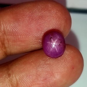 Puede incluir: Primer plano de una piedra preciosa de rubí estrellado rosa con una estrella de seis puntas.