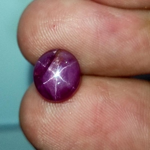 Peut inclure: Une pierre précieuse de rubis étoilé ronde, de couleur violette, avec une étoile à six branches au centre.