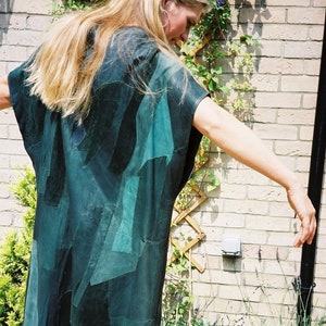 May include: A woman wearing a dark green patchwork jacket made of different pieces of leather. The jacket has a loose fit and a sleeveless design.