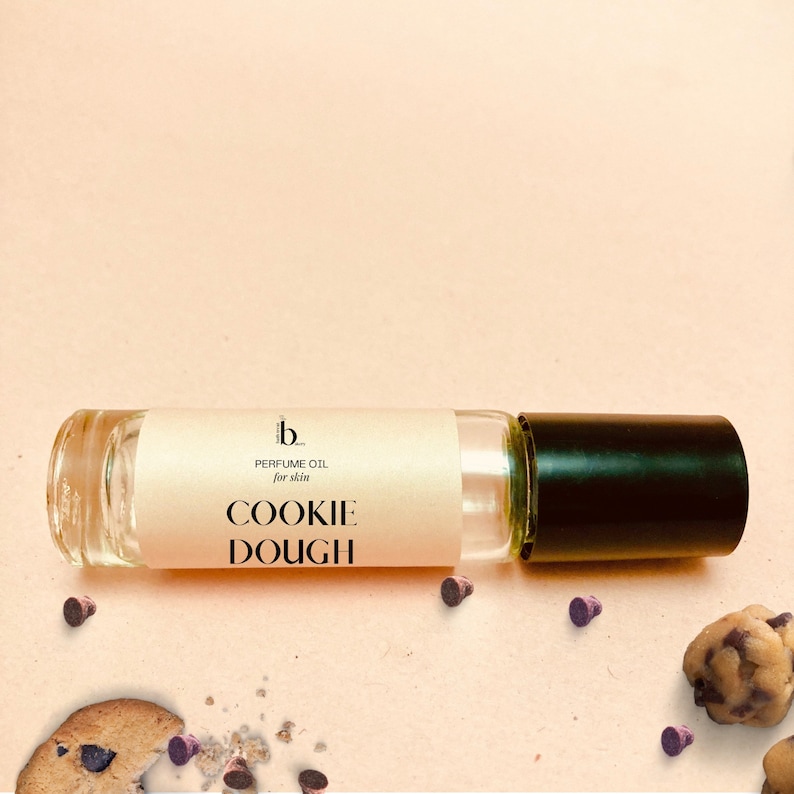 May include: A clear glass roller bottle with a black cap. The label reads "b... PERFUME OIL for skin COOKIE DOUGH".