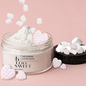 May include: A clear glass jar filled with white dusting powder, topped with marshmallows and heart-shaped cookies with pink polka dots. The jar has a black lid and the text "TOO SWEET". The jar contains 4oz (118 ml) of product.