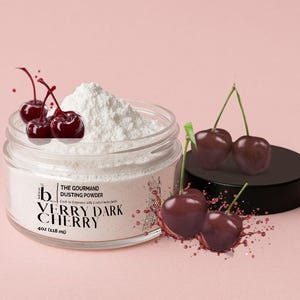May include: A clear glass jar filled with white dusting powder, labeled "VERRY DARK CHERRY." The jar is surrounded by ripe, dark red cherries and splashes of cherry juice. The product is 4oz (118 ml).