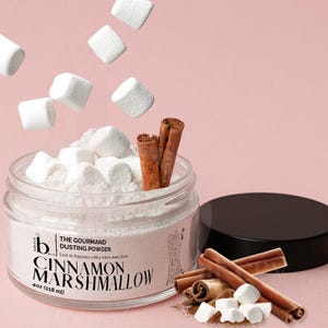 May include: A clear glass jar of Cinnamon Marshmallow dusting powder with marshmallows and cinnamon sticks. The jar has a black lid and the label reads "The Gourmand Dusting Powder" and "Cinnamon Marshmallow". The jar contains 4 oz (118 ml) of product.