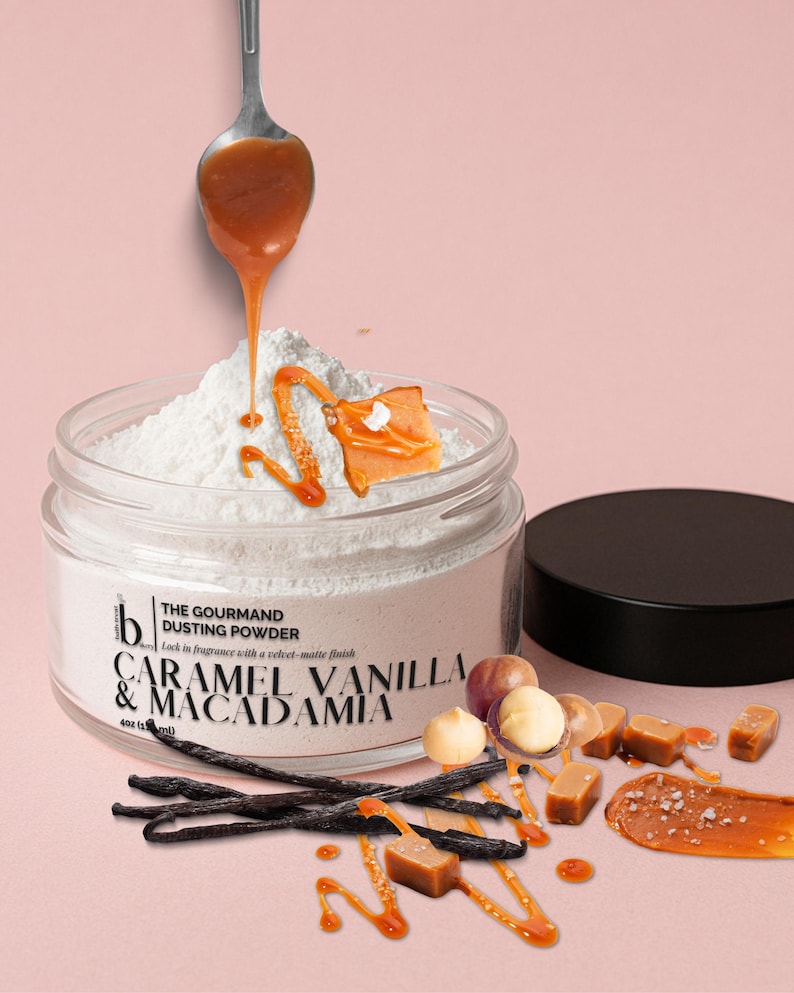 May include: A jar of "The Gourmand Dusting Powder" with caramel, vanilla, and macadamia flavour. Caramel sauce drips from a spoon onto the white powder. Vanilla beans, macadamia nuts, and caramel sweets are scattered around the jar.