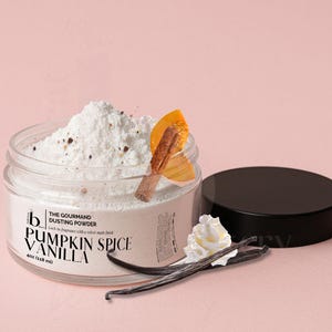 May include: A clear jar of Pumpkin Spice Vanilla dusting powder with a black lid. The label reads The Gourmand Dusting Powder, 4oz (118 ml). The powder is topped with a cinnamon stick, a slice of pumpkin, a dollop of whipped cream, and vanilla beans.