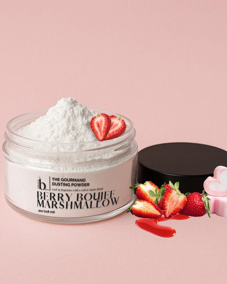 May include: A glass jar containing white dusting powder, with the label "Berry Boujee Marshmallow." Fresh strawberries and a black lid are next to the jar. The text reads "The Gourmand Dusting Powder."