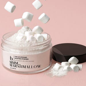 May include: A clear glass jar filled with white dusting powder and marshmallows, with some marshmallows floating above. The jar has a black lid and the text "MMM... MARSHMALLOW" on the label. The jar contains 4 oz (118 ml) of product.