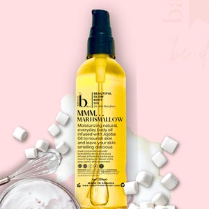 Peut inclure: Une bouteille d'huile pour le corps jaune avec un bouchon noir. L'étiquette indique "BEAUTIFUL GLOW BODY OIL" et "MMM... MARSHMALLOW". La bouteille est entourée de guimauves et d'un fouet. Contient 125ml.