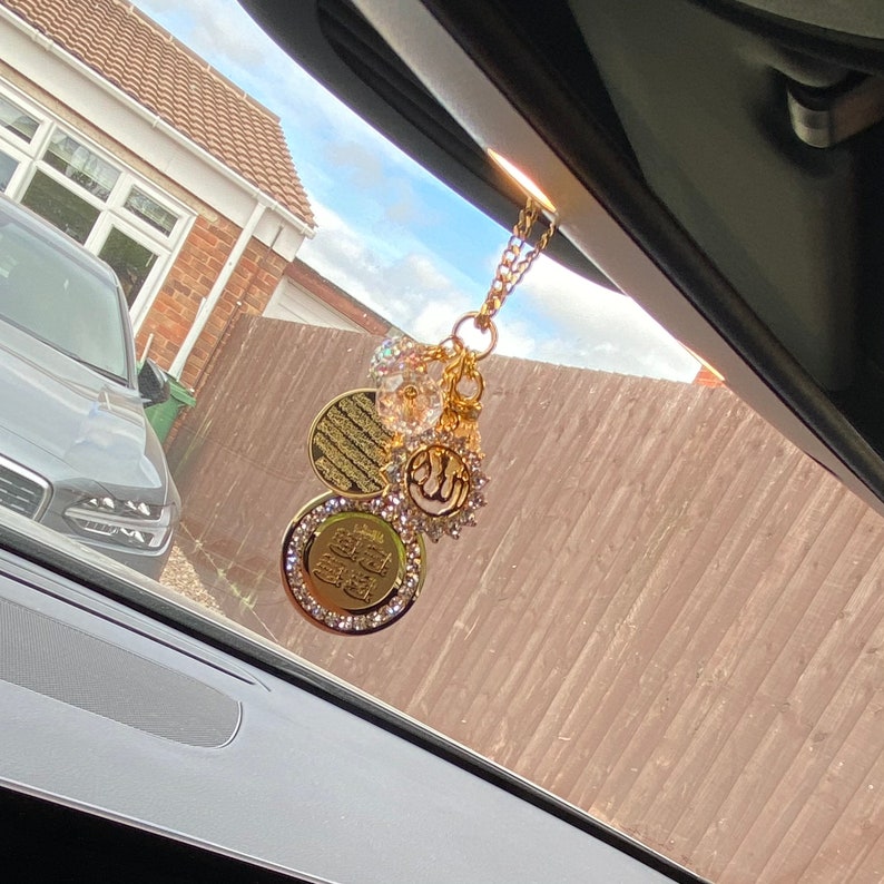 May include: Gold car charm with a chain, featuring a clear crystal bead, a round charm with Arabic script, a star-shaped charm with a crescent moon and a round charm with Arabic script and rhinestones.