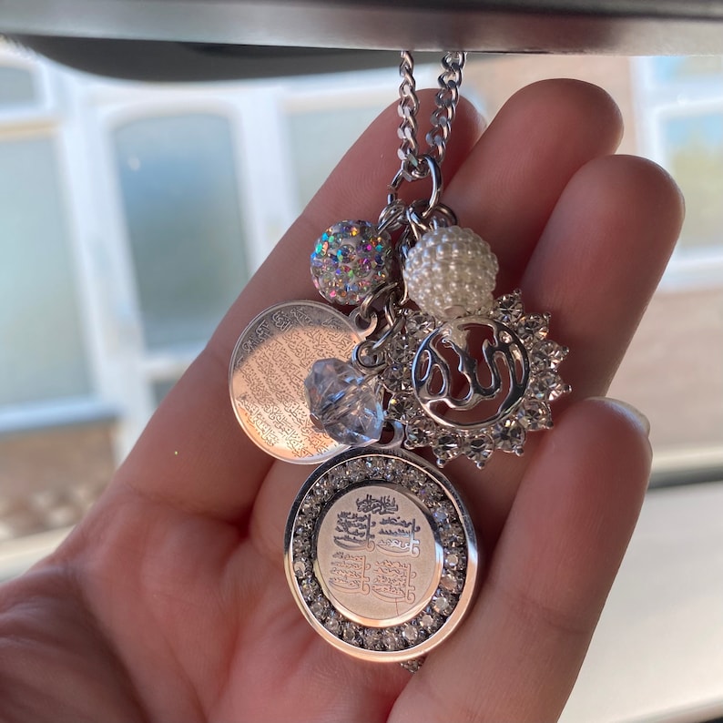 May include: A silver car charm with a chain, a round charm with Arabic script, a round charm with a sparkly design, a round charm with a white pearl, and a round charm with a silver Allah symbol.