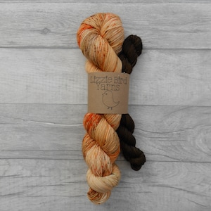 May include: Two skeins of yarn, one orange and brown speckled and one brown, wrapped together with a brown paper label that reads "Lizzie Bird Yarns" and a small bird illustration.