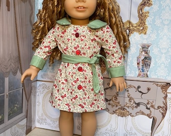 Könnte beinhalten: Eine Puppe mit langen, lockigen, rotbraunen Haaren und grünen Augen, die ein Kleid mit Blumenmuster, roten Knöpfen und einem grünen Kragen und Gürtel trägt. Die Puppe trägt auch weiße Schuhe.