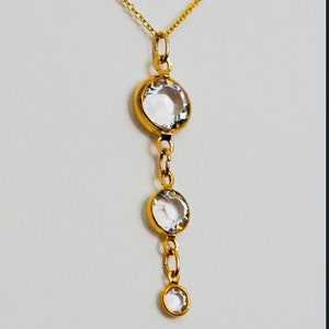 May include: A gold chain necklace with three clear round stones hanging from it. The stones are set in gold.