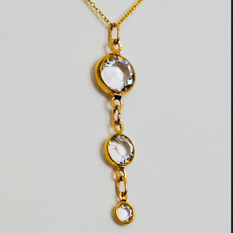 May include: A gold chain necklace with three clear round stones hanging from it. The stones are set in gold.
