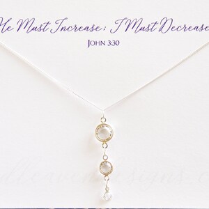 May include: A silver necklace with a pendant featuring three clear crystal stones. The necklace has a delicate chain and the pendant is a simple design. The text "He Must Increase: I Must Decrease" and "JOHN 3:30" is printed on a white card behind the necklace.