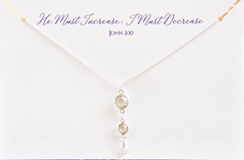 May include: A silver necklace with a pendant featuring three clear crystal stones. The necklace has a delicate chain and the pendant is a simple design. The text "He Must Increase: I Must Decrease" and "JOHN 3:30" is printed on a white card behind the necklace.