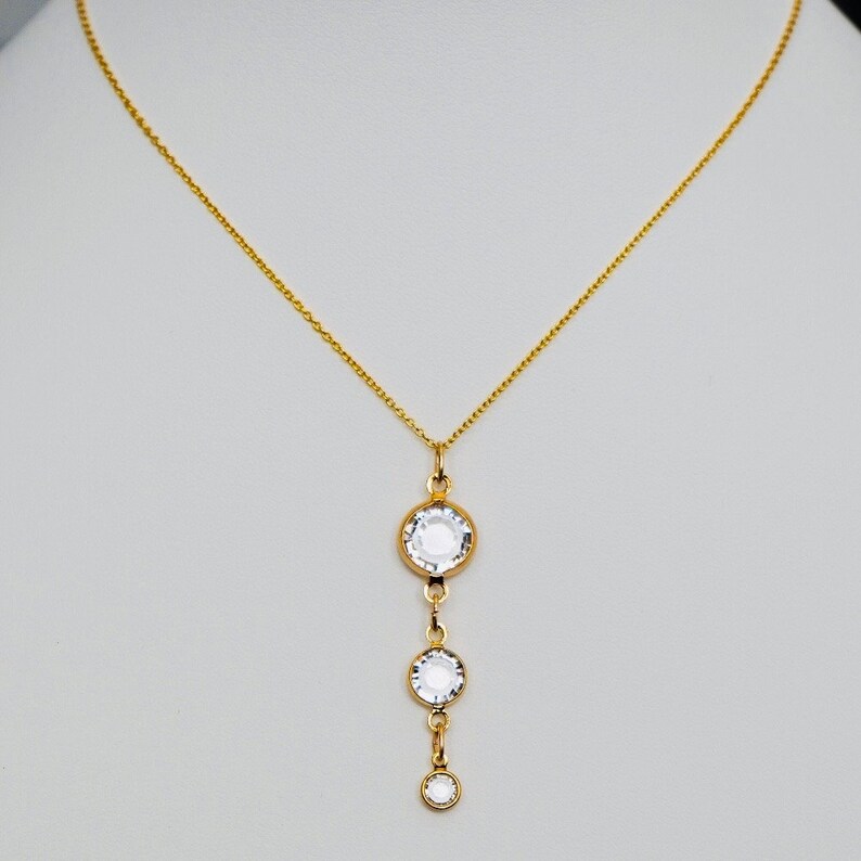 May include: A gold chain necklace with a pendant featuring three clear round crystals.