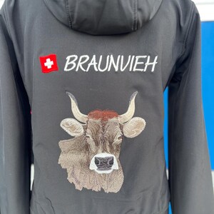 Könnte beinhalten: Schwarze Kapuzenjacke mit gesticktem Design. Mit Schweizer Flagge und dem Wort "BRAUNVIEH" in Weiß. Darunter ein gesticktes Bild eines braunen Kuhkopfes.