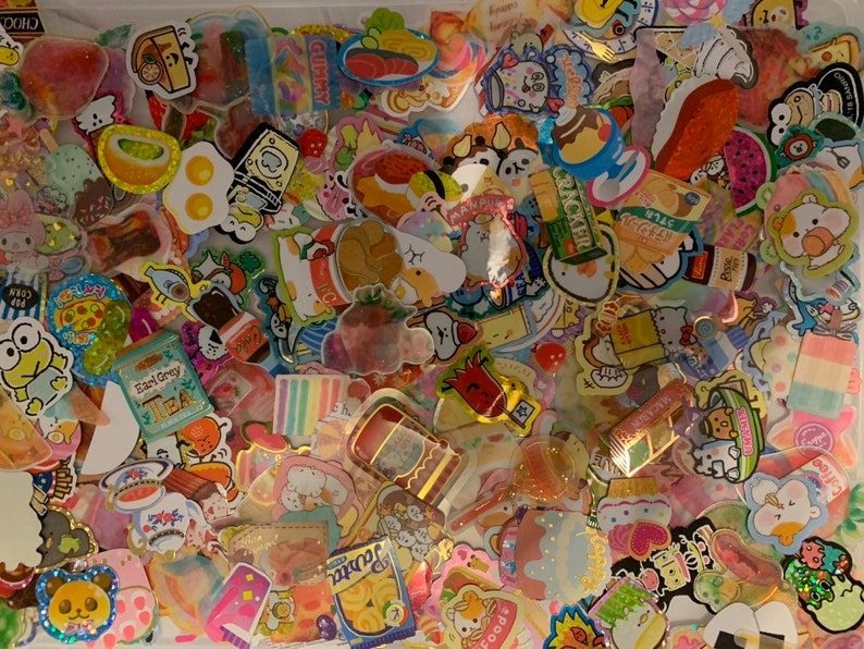May include: A large collection of colorful and whimsical stickers featuring cartoon characters, food, and other cute designs. The stickers are arranged in a random pattern and are perfect for decorating journals, laptops, or other personal items.