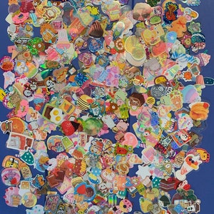 May include: A large collection of colorful, sparkly, and holographic stickers featuring various cute cartoon characters, food, and other designs. The stickers are arranged in a random pattern on a blue surface.