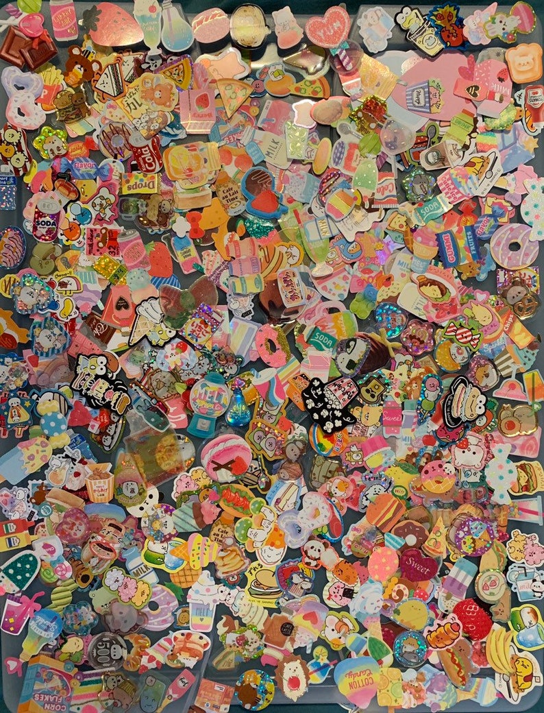 May include: A large collection of colorful stickers featuring various food and drink themes. The stickers are mostly round or square and feature cartoon characters, text, and illustrations. Some of the stickers have glitter or holographic finishes. The stickers are arranged in a random pattern on a blue surface.