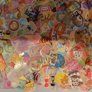 May include: A collection of colorful stickers featuring various designs, including food, animals, and text. The stickers are arranged in a random pattern and are mostly on a white background.