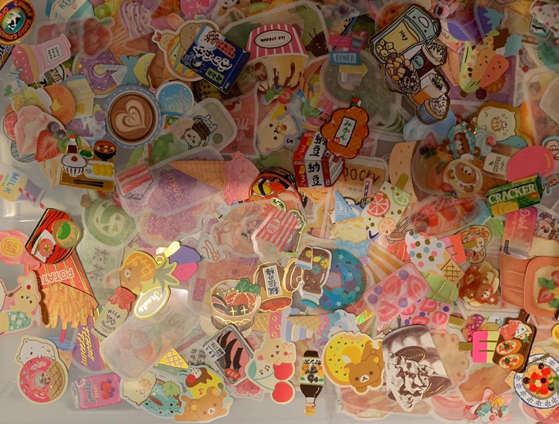 May include: A collection of colorful stickers featuring various designs, including food, animals, and text. The stickers are arranged in a random pattern and are mostly on a white background.