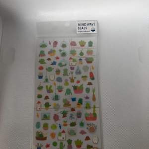 May include: A clear plastic sheet of small, colourful stickers featuring various cacti, succulents, and potted plants in different containers. The header label reads MIND WAVE SEALS Original designs, and a small sign at the bottom says Taniku Seikatsu.