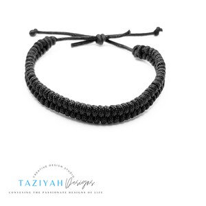 May include: A black braided bracelet with adjustable closure. The bracelet is made of a thick, durable cord.