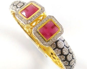 May include: Gold bangle bracelet with two red gemstone accents surrounded by clear stones. The bracelet has a black and white honeycomb design.