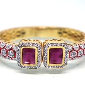 Puede incluir: Pulsera rígida de oro con un patrón geométrico rojo y blanco y dos piedras cuadradas de color rojo rubí engastadas en oro.