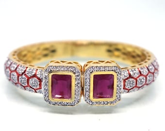 May include: Gold bangle bracelet with a red and white geometric pattern and two square-shaped ruby red stones set in gold.