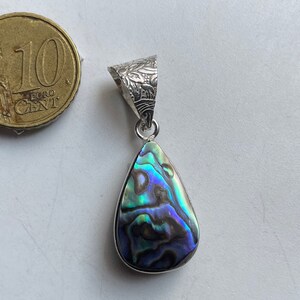 Könnte beinhalten: Ein silberner Anhänger mit einem tropfenförmigen Abalone-Muschelschmuck. Die Muschel hat schillernde Farben in Blau, Grün und Lila.