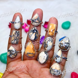 May include: A collection of ten silver rings with various brown, white, and black gemstone settings. The rings are displayed on a hand.