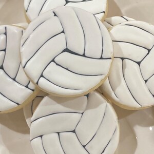 May include: A stack of white and black volleyball-themed cookies. The cookies are decorated with black icing to resemble a volleyball.