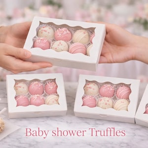 May include: Several boxes of baby shower truffles are displayed. The truffles are pink and white, some with sprinkles or striped designs. Two cake pops are also visible. The text "Baby shower Truffles" is written in pink.