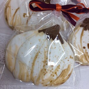 May include: White pumpkin-shaped cookies with brown accents and a chocolate stem, individually wrapped in clear cellophane. Tied with a purple and orange ribbon, these treats are perfect for fall or Thanksgiving.