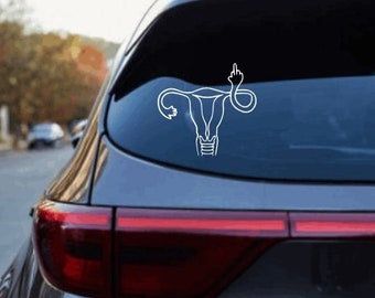Puede incluir: Adhesivo de vinilo blanco de un útero con el dedo corazón levantado, aplicado en la luneta trasera de un coche. El diseño es un dibujo lineal, y el coche es gris oscuro.