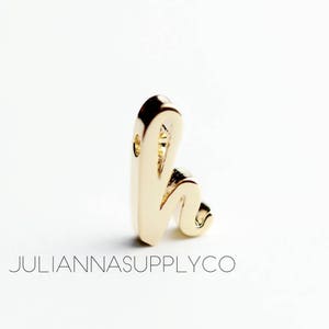 May include: Gold charm in the shape of the letter 'h' in a cursive font.